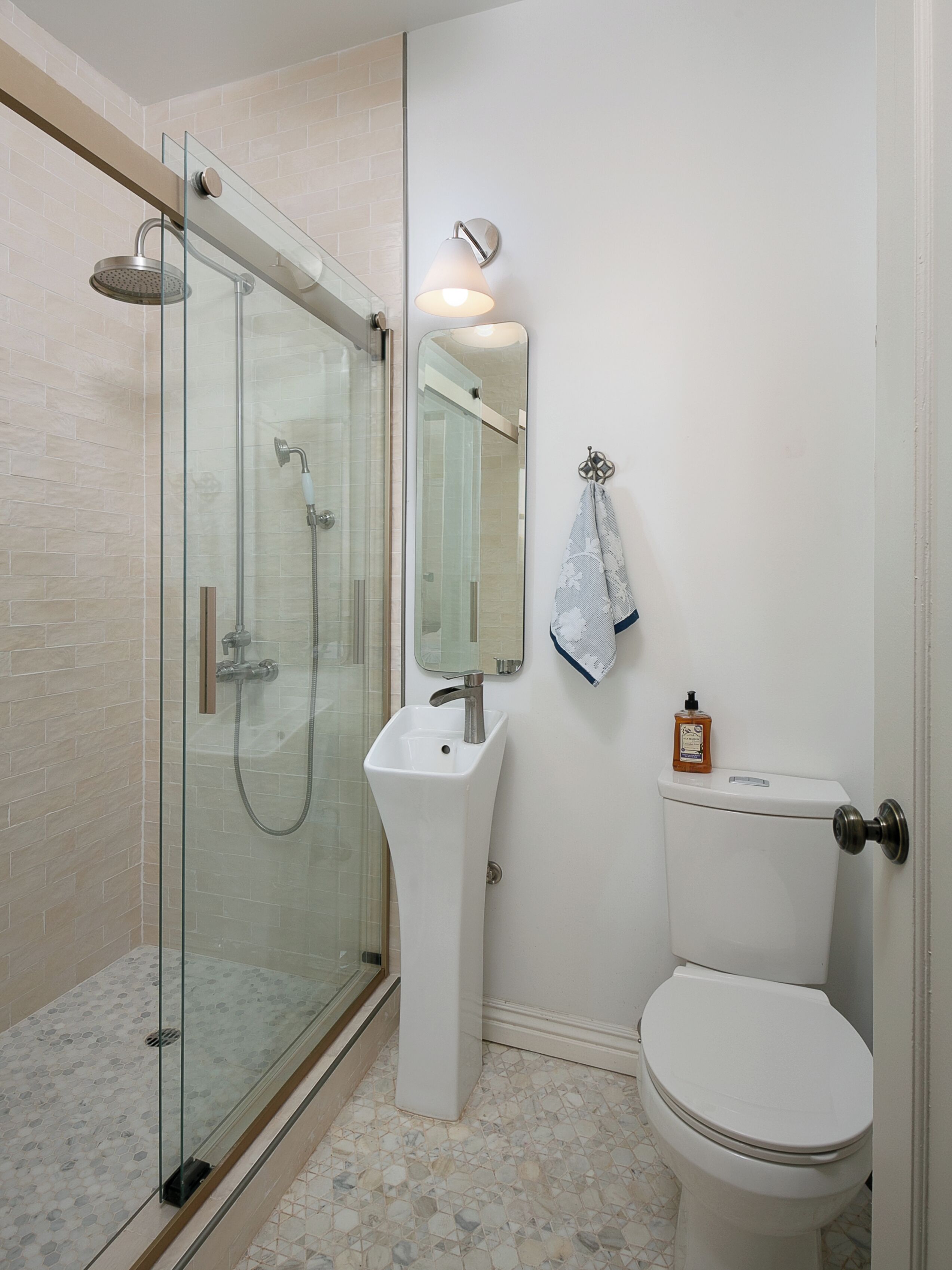 A bathroom with a glass-enclosed shower, a pedestal sink, a toilet, and a mirror.
