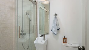 Et badeværelse med bruseniche, et konsolbord med håndvask, toilet og et spejl.
