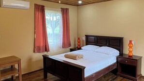 Una habitación con paneles de madera, una cama, un ventilador de techo, un equipo de aire acondicionado y una ventana con cortinas.