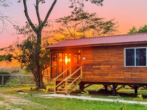 Une cabane en bois avec un toit en métal, un escalier menant à l’entrée et, en arrière-plan, une vue sur le coucher du soleil.