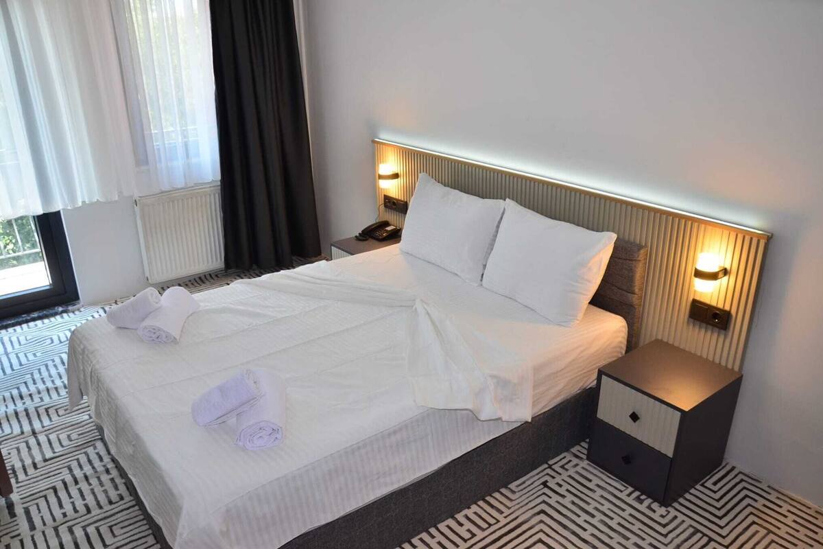 Ein Hotelzimmer mit einem aufgeräumten Bett, zwei Nachttischlampen, einem Nachttisch und einem gemusterten Boden.