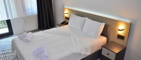 Habitación de hotel con una cama bien hecha, dos lámparas de noche, una mesita de noche y un suelo estampado.