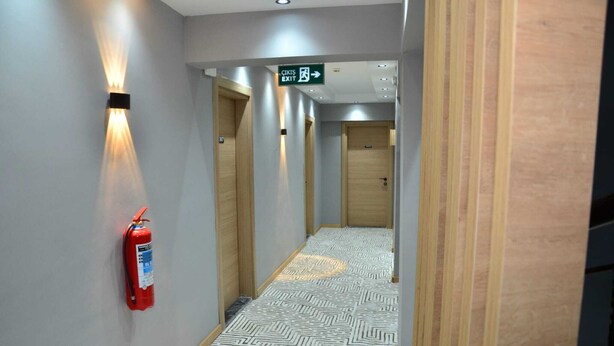 A hallway with patterned flooring, wooden doors, and a fire extinguisher mounted on the wall. - ARGUN OTEL (Aydin)