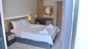 A hotel room with a large bed, a bedside table, a mirror, and a wooden panel wall. - ARGUN OTEL (Aydin)