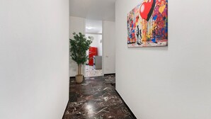 Een gang met een marmeren vloer, een kamerplant en een kleurrijk abstract schilderij aan de muur.