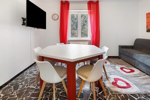 Una habitación con una mesa blanca, cortinas rojas, un sofá gris y una alfombra estampada.