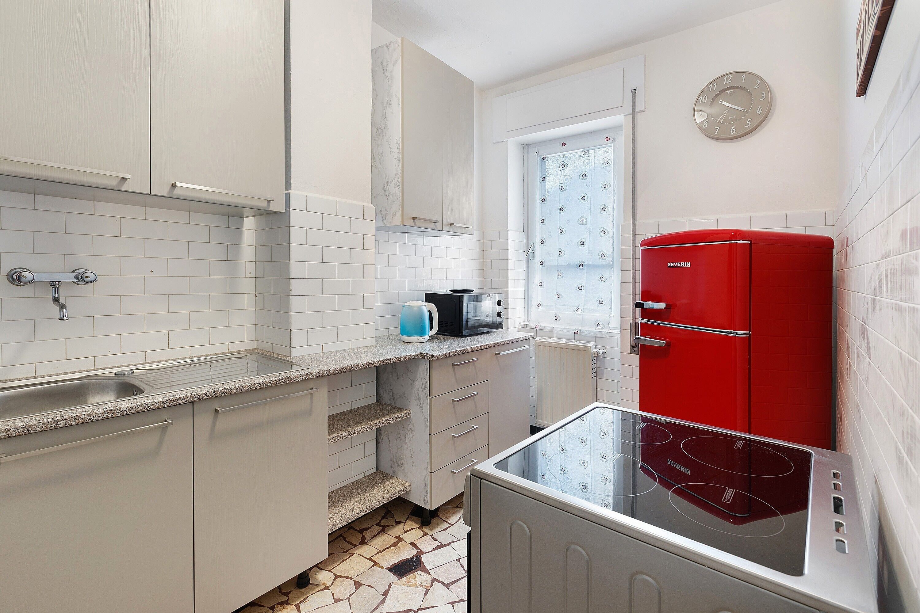 A compact kitchen with a sink, stove, and red refrigerator.