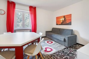 Una habitación con una mesa de comedor, sillas, un sofá, un cuadro y una alfombra estampada.