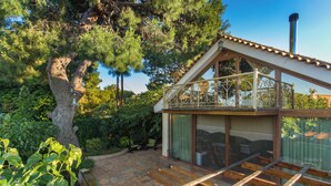 Une maison moderne dotée d’un balcon en verre, d’une terrasse en pierre et d’un grand arbre.