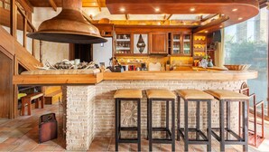 Une cuisine rustique dotée d’une grande cheminée, de tabourets de bar en bois et d’un îlot central en briques.