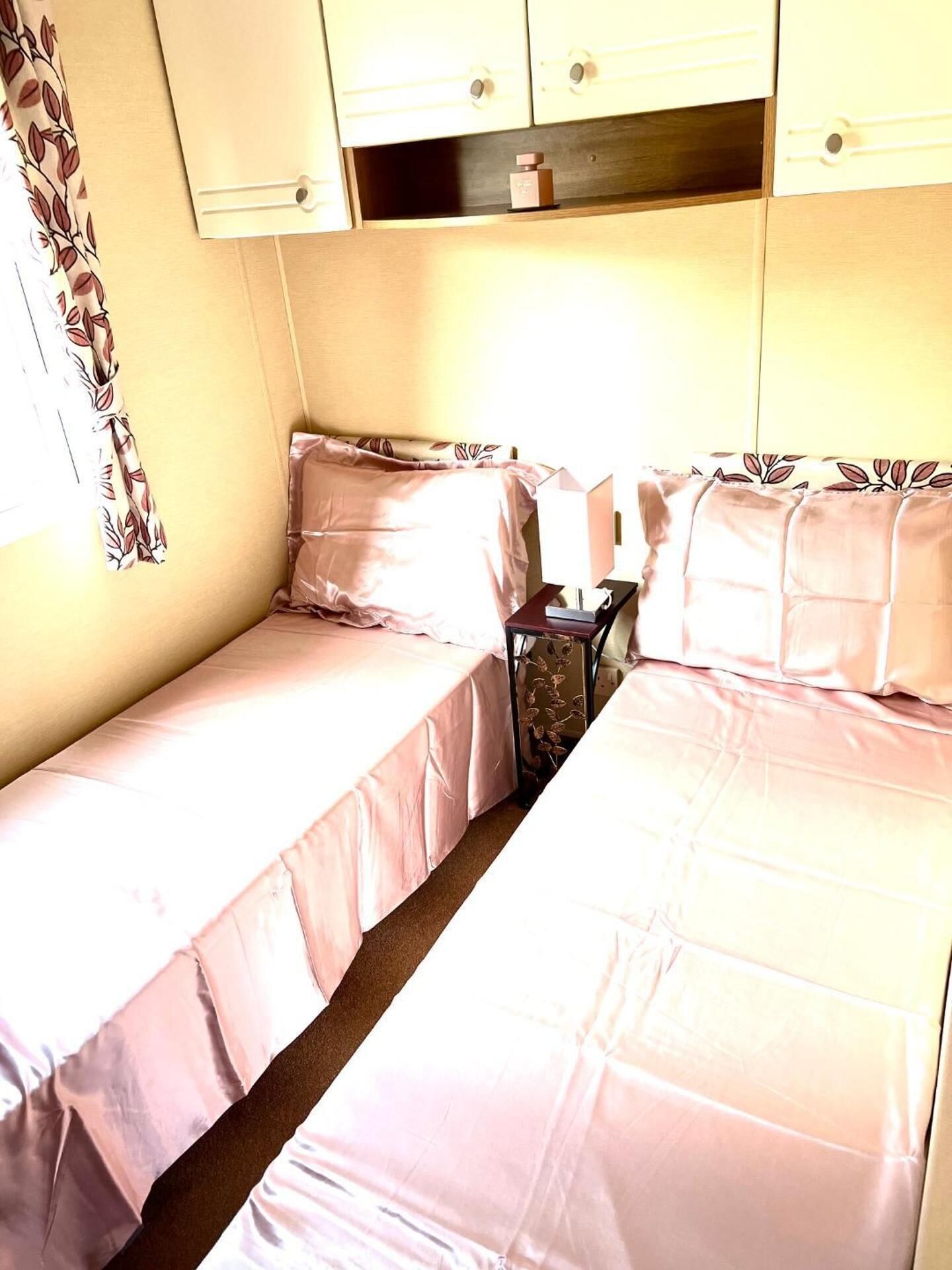 A small, single-room accommodation with two beds, a bedside table, and a cabinet above the beds.