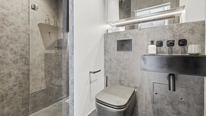 Moderni kylpyhuone, jossa on lasinen suihkuseinä, wc, peilillä varustettu pesuallas ja pyyhekoukku.