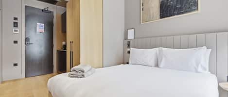 Habitación de hotel con cama, armario, escritorio y un cuadro en la pared.