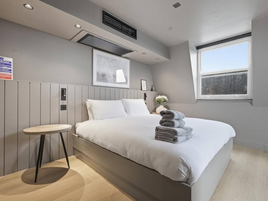 Un dormitorio moderno con cama, mesita de noche y ventana.