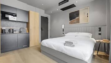 A modern hotel room with a bed, a kitchenette, and a painting on the wall.