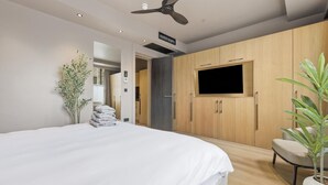 Een moderne slaapkamer met een bed, een televisie, houten kastjes, een plafondventilator en een potplant.