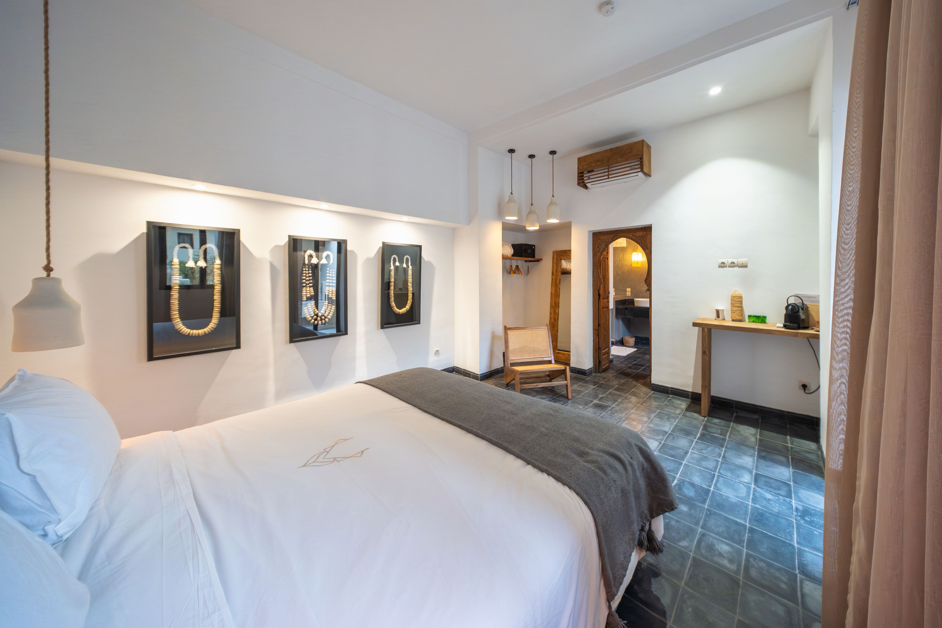 Habitación de hotel con cama, una obra de arte en la pared, una silla, una mesita y un baño visible a través de una puerta abierta.