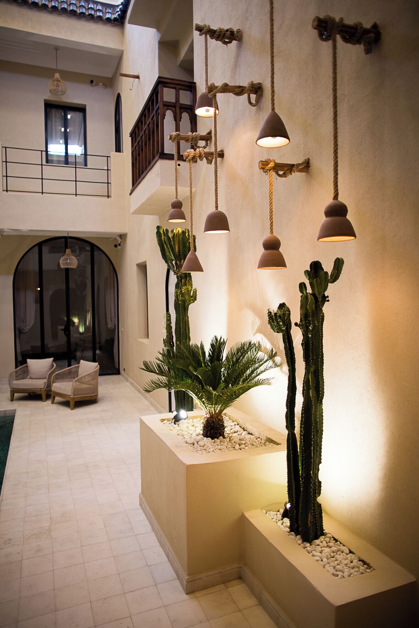 Un espacio interior amplio con techo alto, varias lámparas colgantes y una zona de estar con sillas.