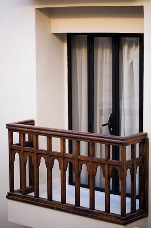 Un balcón de madera con barandilla, una ventana con cortinas y una puerta.