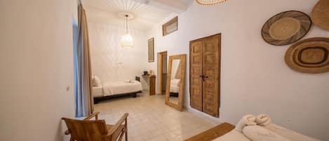 A bedroom with a bed, a wooden chair, a wooden wardrobe, a mirror, and a hanging light fixture.