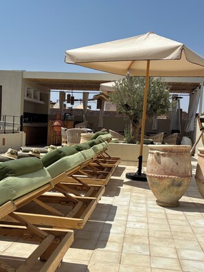 Una terraza en la azotea con sillones de descanso, una jardinera grande y una pérgola con sombrillas.