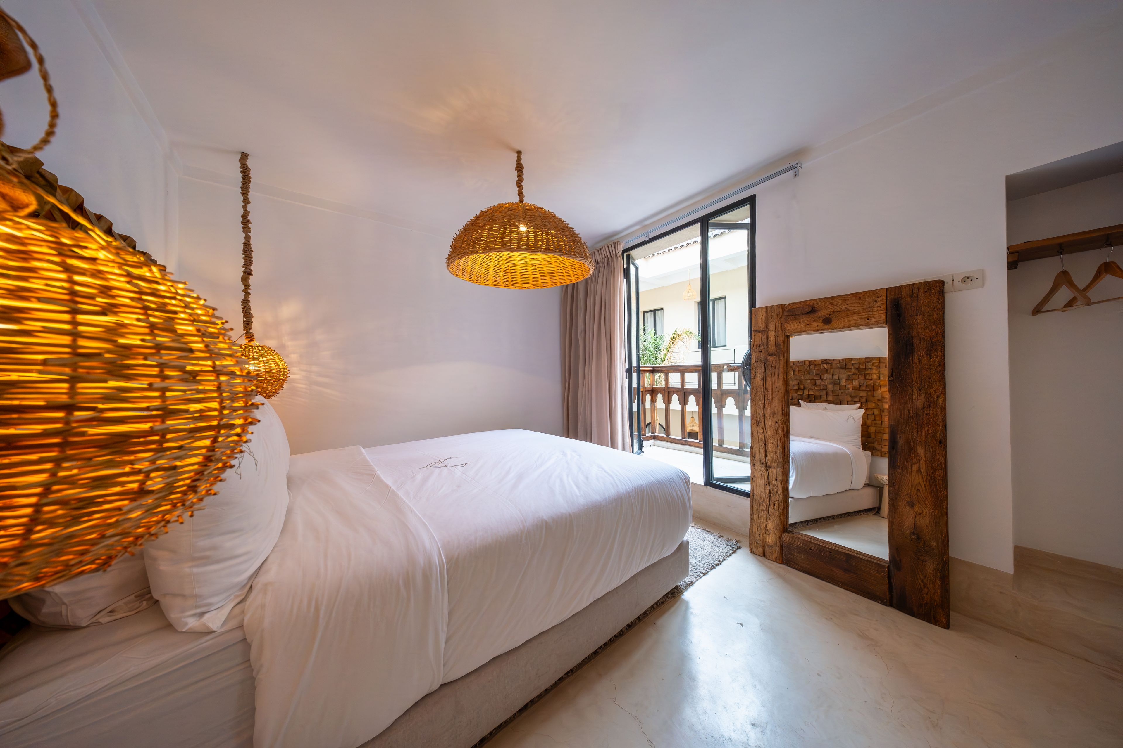 A bedroom with a large bed, a hanging light fixture, a wooden headboard, and a view of the outside.