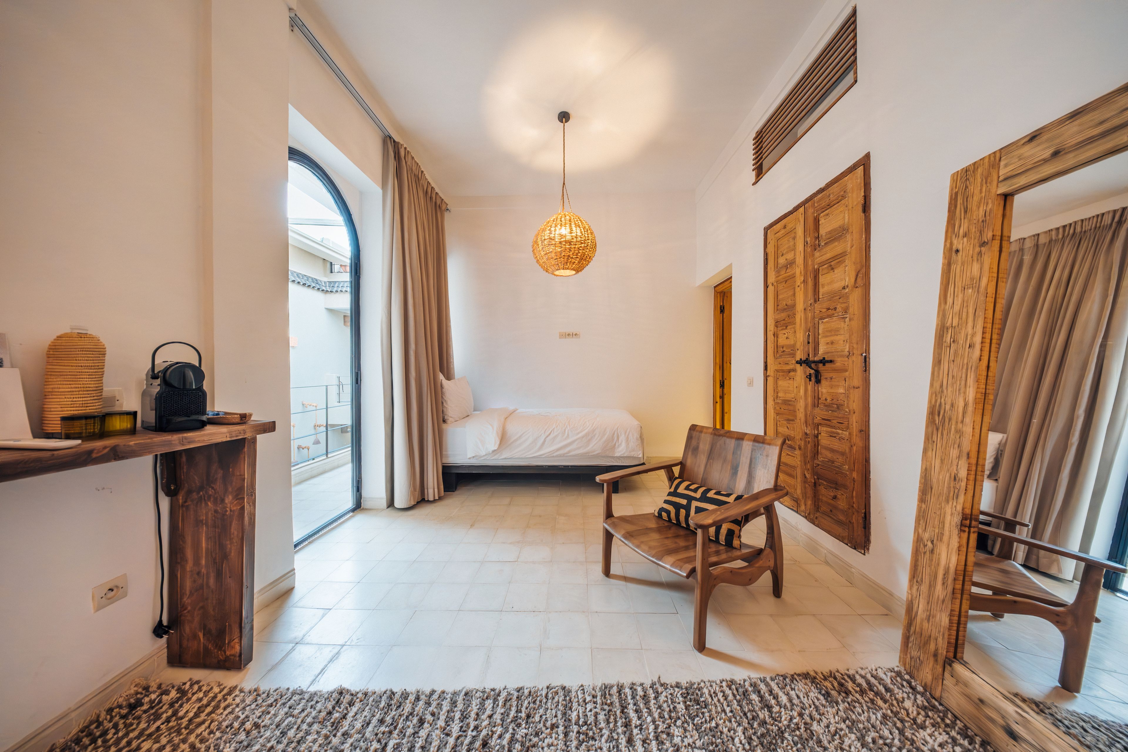 Una habitación de hotel con una cama, una silla, un escritorio, una lámpara colgante y un ventanal grande.
