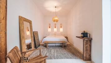 Un dormitorio con cama, una silla de madera, un espejo, una mesita de noche y una lámpara colgante.