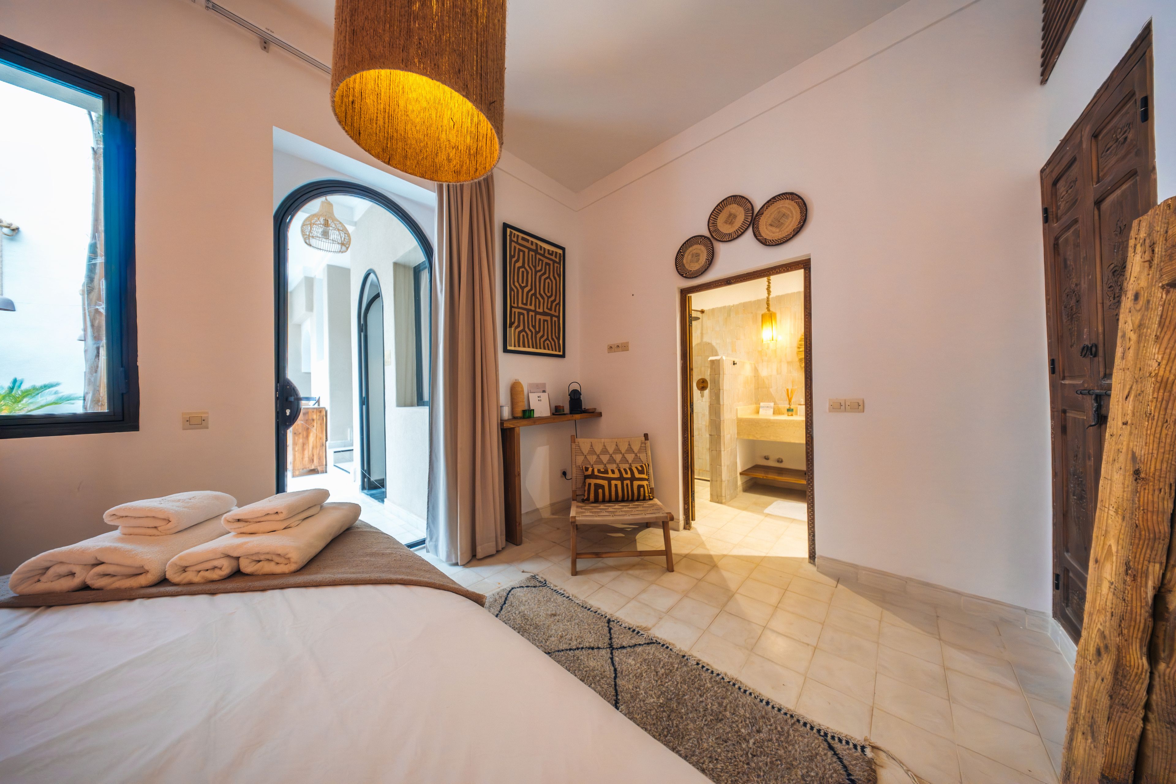 A hotel room with a bed, a chair, a wooden door, and a bathroom visible through an open door.