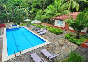 A rectangular pool with clear blue water, surrounded by stone tiles. There are lounge chairs and umbrellas around the pool. - Coconut Lodge (Las Cumbres)