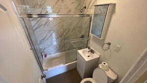 Een badkamer met een glazen douchecabine, een witte wastafel, een toilet en een spiegel boven de wastafel.