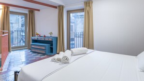 A hotel room with a bed, a blue dresser, a small table with a vase, and a balcony with a railing. - Casa DAS Vacation Home – Modica, Baroque City (Modica)