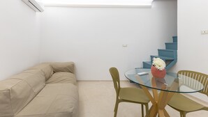 A room with a beige sofa, a glass table with chairs, a vase with flowers, and a blue staircase. - Casa DAS Vacation Home – Modica, Baroque City (Modica)