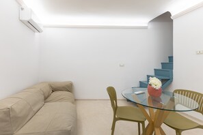 Ein Zimmer mit einem beigefarbenen Sofa, einem Glastisch mit Stühlen, einer Vase mit Blumen und einer blauen Treppe.