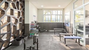 A gym with weightlifting equipment, benches, and a large window with a view of palm trees.