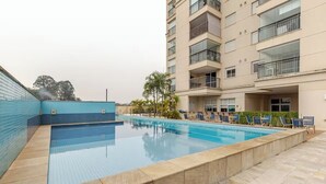 A swimming pool with tiled edges, lounge chairs, and a multi-story building with balconies.