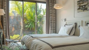 Un dormitorio con una cama, un escritorio con lámpara, una silla y vistas a zonas verdes al exterior.