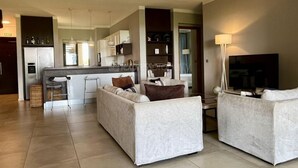 Una sala de estar moderna con un sofá, un televisor y una zona de cocina al fondo.