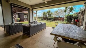 Un espacio de sala-comedor abierto con una mesa de comedor y dos sofás, un ventilador de techo y vistas al jardín.