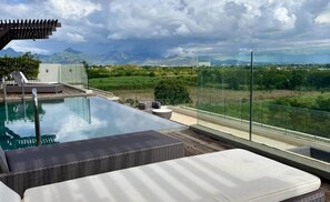 A rooftop infinity pool with a glass balustrade, wicker lounge chairs, and a view of distant mountains. - Luxurious & peaceful blend villa in Royal Park Balaclava Mauritius 5 (Balaclava)