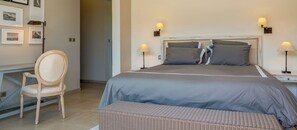 A bedroom with a bed, two bedside lamps, a chair, and a desk with framed pictures. - Luxurious & peaceful blend villa in Royal Park Balaclava Mauritius 5 (Balaclava)