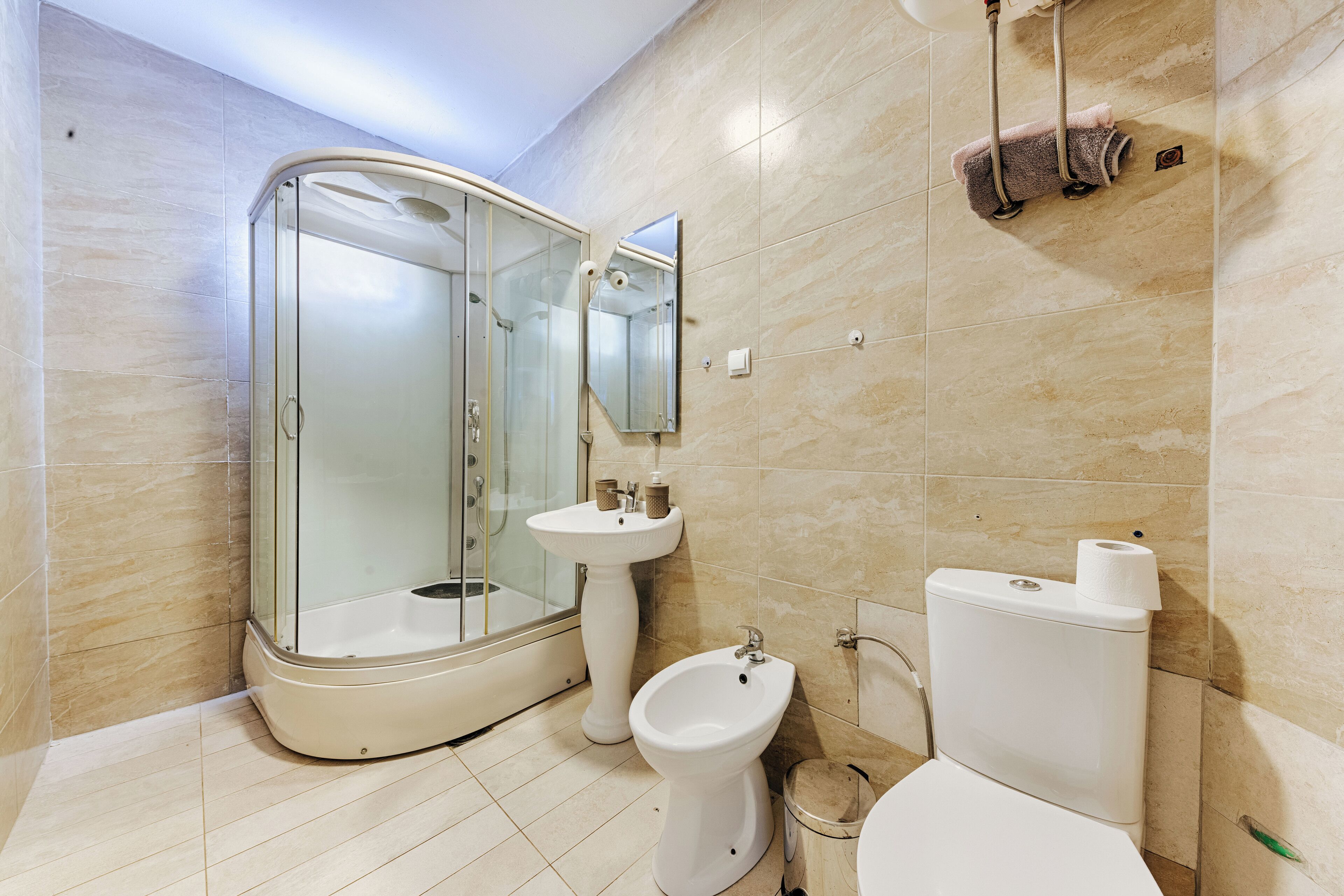 A modern bathroom with a glass-enclosed shower, a pedestal sink, a bidet, and a toilet.