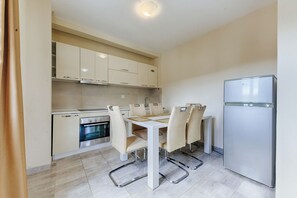 A compact kitchen with a dining table, chairs, a refrigerator, and built-in oven. - Apartman ZIS 3 LUX (Opština Bar)