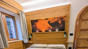 Ein Schlafzimmer mit einem hölzernen Kopfende, einem großen Bett mit kariertem Bettbezug, zwei Nachttischen mit Lampen und einem Fenster mit Vorhängen.