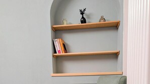 Ein grüner Sessel mit schwarzen Beinen, ein Holzboden und eine graue Wand mit Regalen.