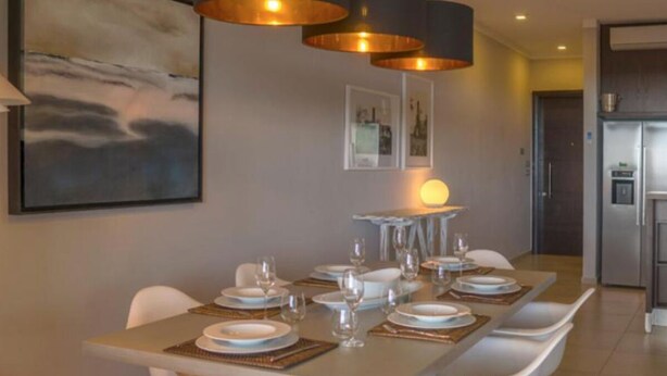 Een eetgedeelte met een lange tafel voor zes personen, witte stoelen en moderne hanglampen.