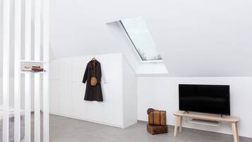 A modern living room with a white wardrobe, a coat hanging on the wall, a television on a wooden stand, and a skylight above.