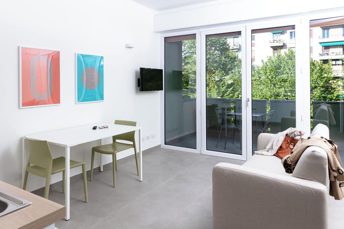 A modern living room with a white sofa, a dining table with chairs, and a TV mounted on the wall.