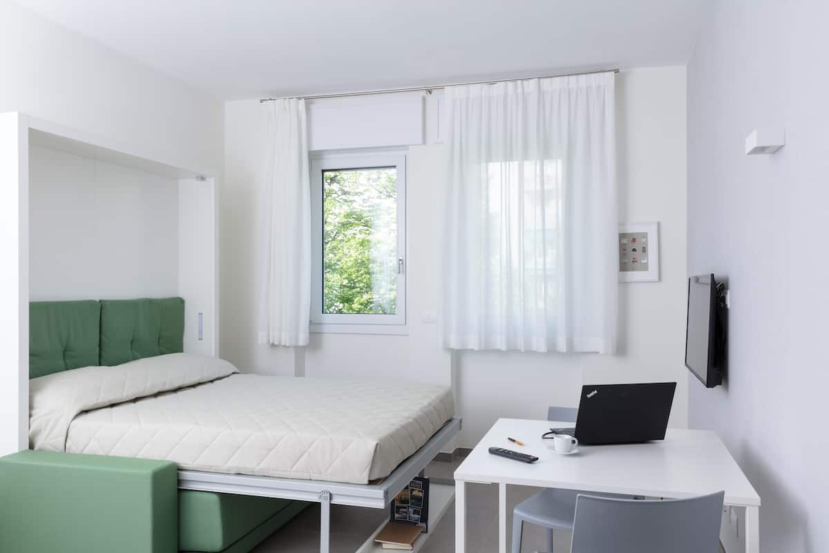 A modern room with a bed, a desk, and a window.