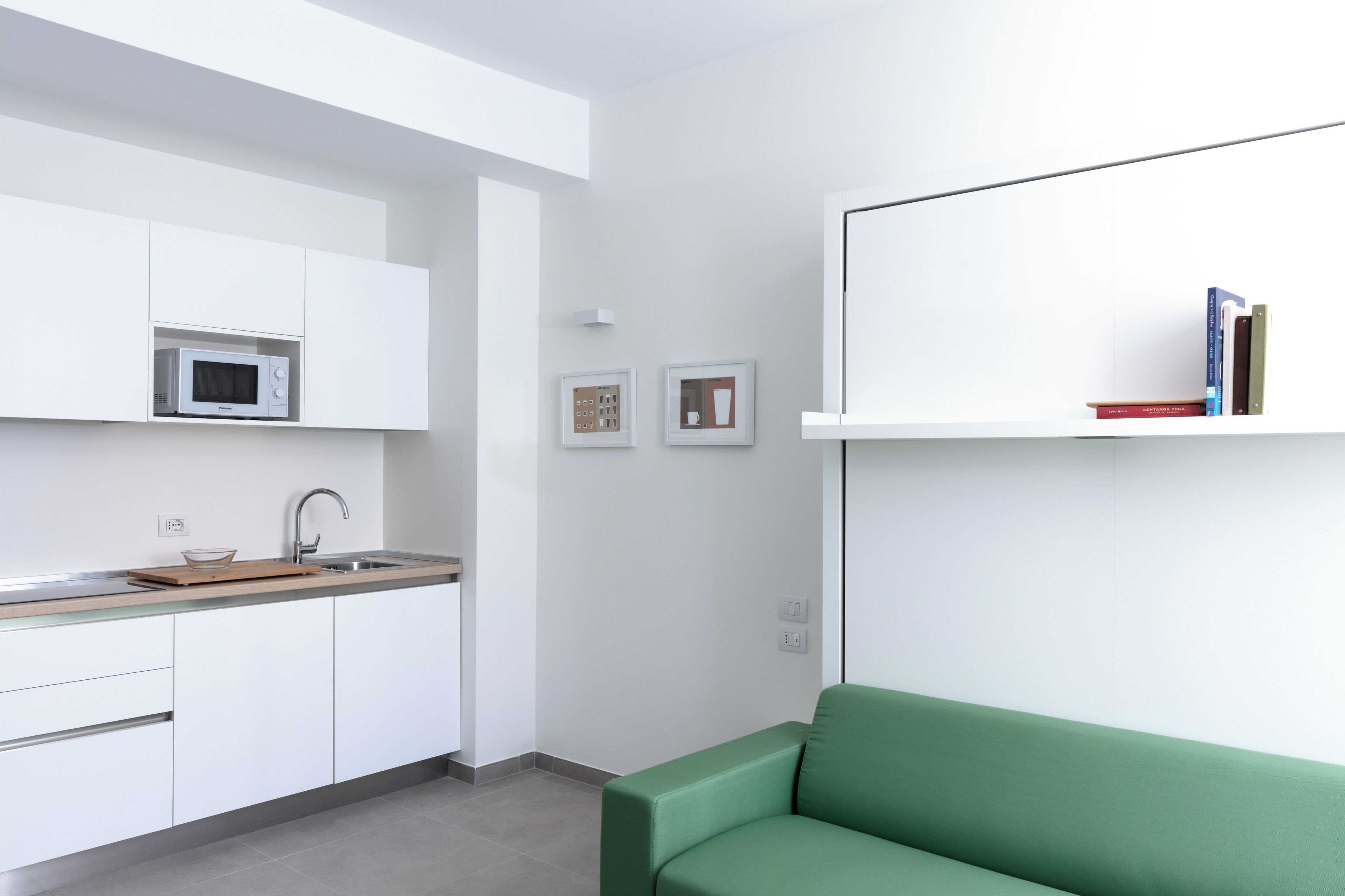 A modern kitchen with white cabinetry, a built-in microwave, and a green sofa in a minimalist living area.
